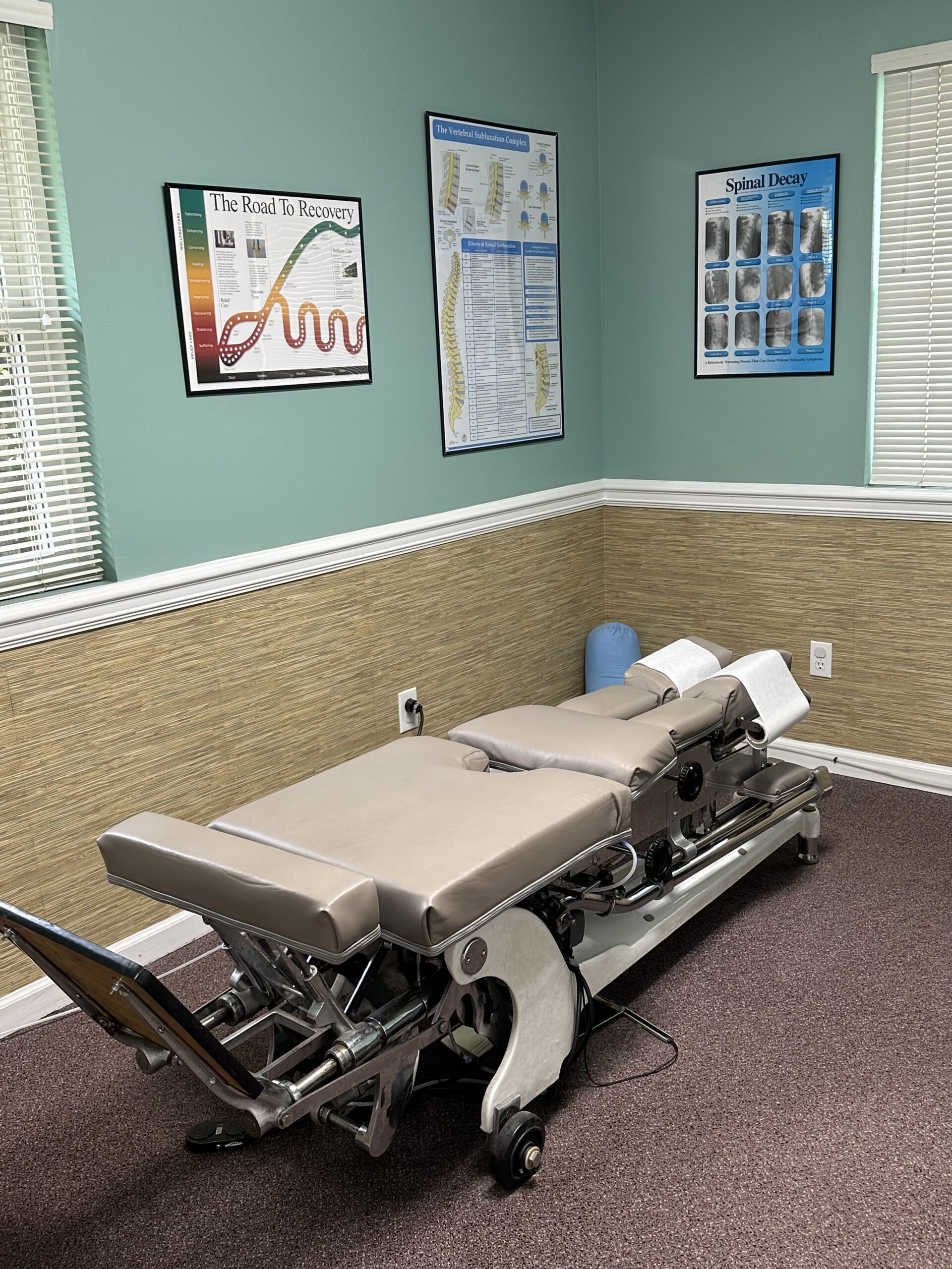 Tan chiropractic table laid flat in teal room.